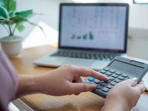Close up of person typing on calculator with laptop open in background for article What Salary Do You Need to Live Comfortably in Denver? (2025) for newcomers moving to Denver.