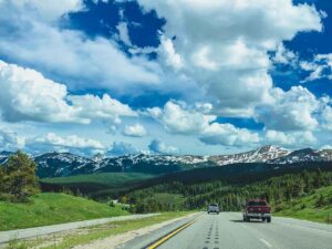 Cars driving on the road in the Rocky Mountains for article How to Register Your Car After Moving to Colorado for newcomers moving to Denver.