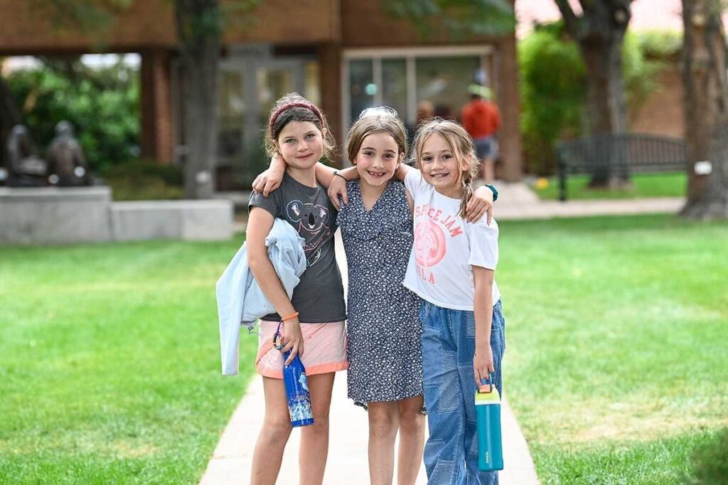 3 Girl students standing in front of school posing for picture for article Denver Academy for newcomers moving to Denver.
